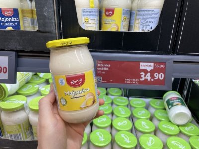 Ruka držící majonézu před regálem supermarketu