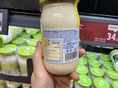 Ruka držící majonézu před regálem supermarketu
