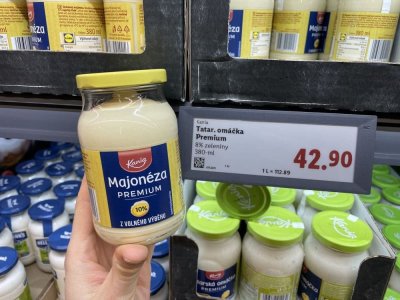 Ruka držící majonézu před regálem supermarketu