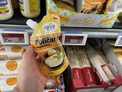 Ruka držící majonézu před regálem supermarketu