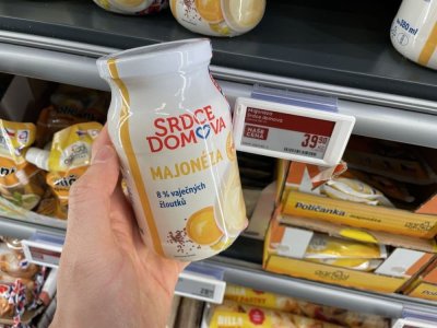 Ruka držící majonézu před regálem supermarketu