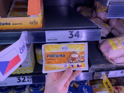 Ruka držící majonézu před regálem supermarketu