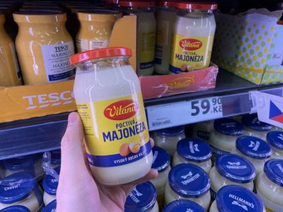 Ruka držící majonézu před regálem supermarketu