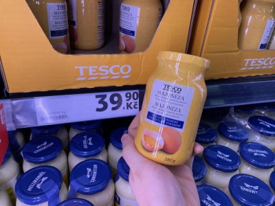 Ruka držící majonézu před regálem supermarketu