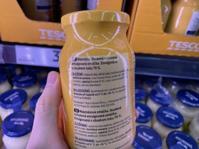 Ruka držící majonézu před regálem supermarketu