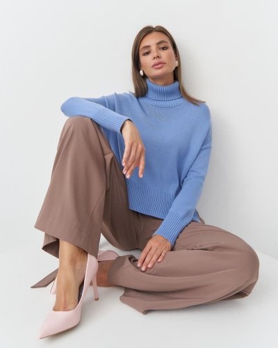 Mladá žena v modrém svetru a hnědých kalhotách