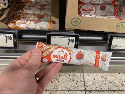 Ruka držící müsli tyčinku před regálem v supermaretu