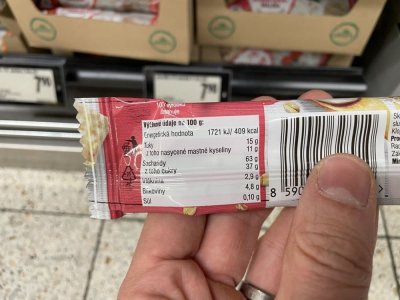 Ruka držící müsli tyčinku před regálem v supermaretu