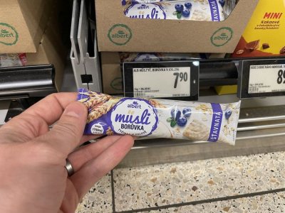 Ruka držící müsli tyčinku před regálem v supermaretu