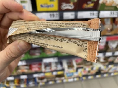 Ruka držící müsli tyčinku před regálem v supermaretu