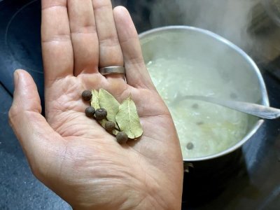 Bobkové listy a nové koření na mužské dlani, v pozadí vroucí nálev v hrnci