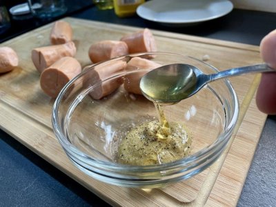 Med a hořčice ve skleněné misce, v pozadí nakrájené špekáčky