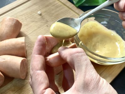 Muž plní špekáčky hořčicí