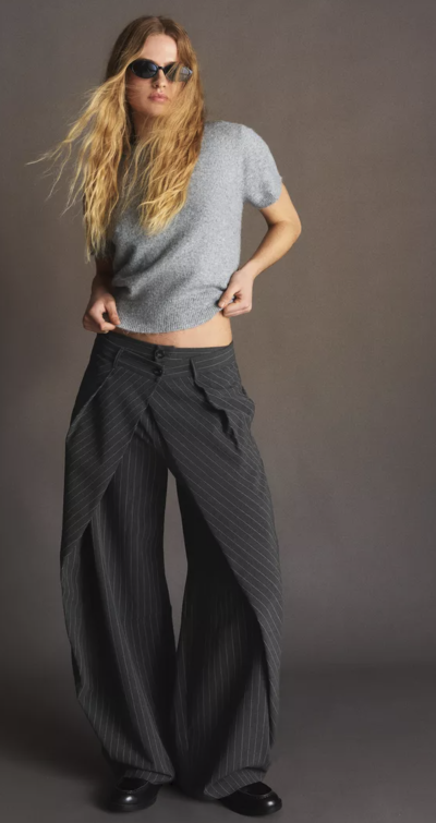 Modelka v šedém tričku a tmavých širokých kalhotách