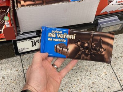 Ruka držící tabulkovou čokoládu před regálem supermarketu