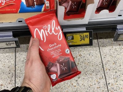 Ruka držící tabulkovou čokoládu před regálem supermarketu