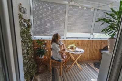 Žena sedí na balkoně zastíněném venkovními roletami.