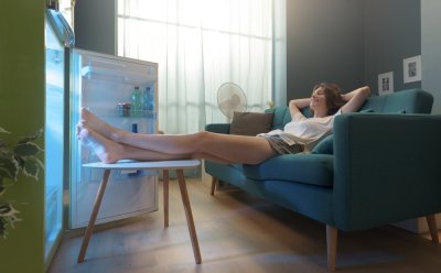Žena sedí na gauči a nohy má u otevřené lednice.