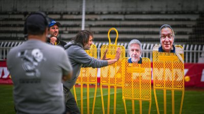 Muž gestikuluje před žlutými stojany s obličeji R. Genzera a M. Suchánka