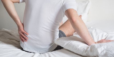 Muž vstává z postele a drží se záda.