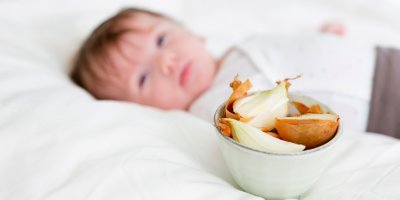 Malý chlapec leží v posteli, vedle něj je miska s cibulí