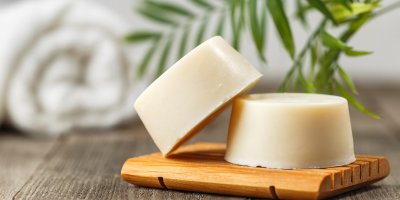 Dva ekologické tuhé šampony bez obalu na dřevěném tácku, v pozadí ručník a rostlina