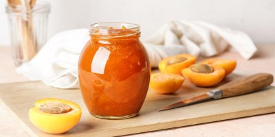 Meruňková marmeláda ve sklenici, rozkrojené meruňky, nůž, prkénko, utěrka