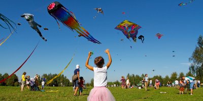 Na obloze jsou desítky draků v různých neobvyklých tvarech a barvách, na travnatém prostranství je spoustu dospělých i dětí