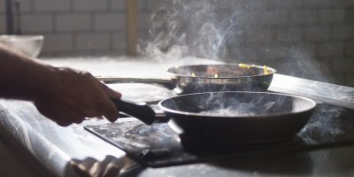 Muž vaří jídlo na dvou pánvích