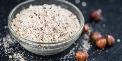 Rozemleté lískové oříšky v misce, vedle celé lískové oříšky