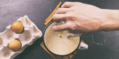 Ruka nad hrnkem s vaječným likérem, vejci a kořením