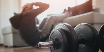 Muž v obývacím pokoji dělá sedy lehy a vedle sebe má činky