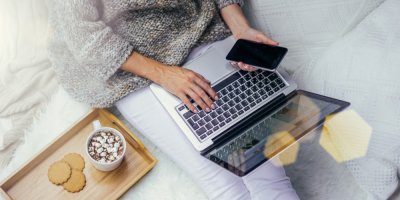 Žena platí za nákupy online v posteli, vedle horký nápoj a sušenky