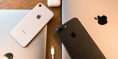 Mobilní telefony iPhone, notebooky Macbook na stole.