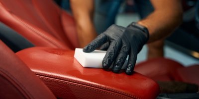 Muž v černých rukavicích utírá pomocí bílé nano houbičky kožené opěradlo.