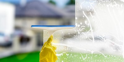 Ruka v rukavici stírající vodu z okna při mytí