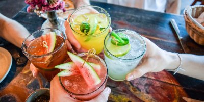 Čtyři lidé si přiťukávají koktejly s melounem, limetkou