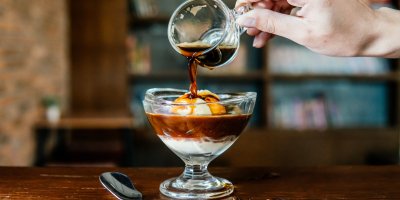 Pohár s kávou a vanilkovou zmrzlinou, do kterého člověk přilévá kávu