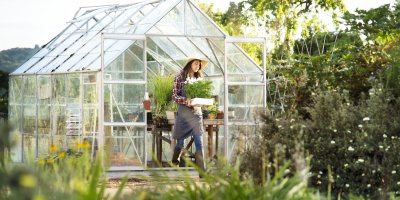 Žena v klobouku přenáší rostlinu ze skleníku ven