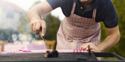 Muž v zástěře čistí kartáčem zahradní gril