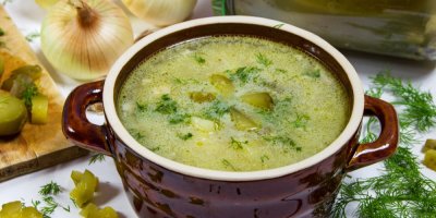 Okurková polévka v keramickém hrnečku, okolo je cibule, kopr a nakládané okurky