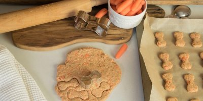 Rozválené těsto, formička ve tvaru kosti, vedle plech s vykrojenými tvary a miska mrkve