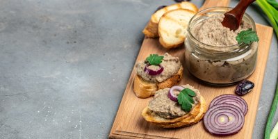 Pomazánka ve sklenici, dva plátky bagety namazané pomazánkou, na nich jsou kolečka červené cibule a bylinky