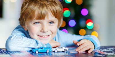 Chlapec si hraje se dvěma malými autíčky, v pozadí jsou vánoční světýlka