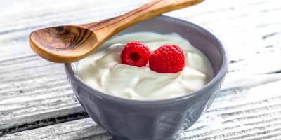 Řecký jogurt a dvě maliny v mističce, dřevěná lžíce