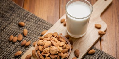 Mandlové mléko ve sklenici, neloupané mandle v misce na prkénku