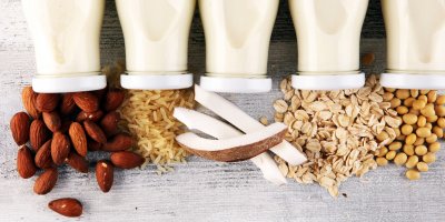 Pět skleněných lahví mléka a pod nimi jsou mandle, rýže, kokos, vločky