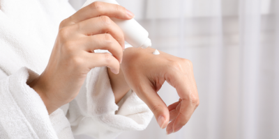 Žena v županu si nanáší krém na hřbet ruky