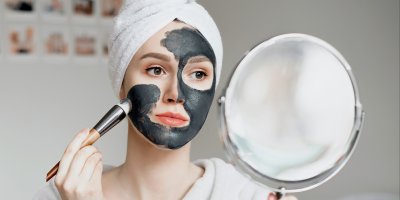 Žena si aplikuje pleťovou masku z černého uhlí před zrcadlem