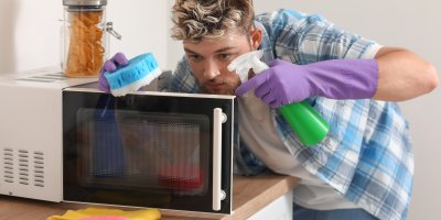 Muž v rukavicích čistí mikrovlnku houbičkou a postřikovačem